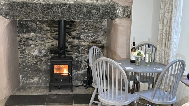 A stone fireplace with a wood-burning stove, a round table with chairs, and a bottle of wine on the table. - Tryfan Cottage  -  2.8 miles from Summit of Mt Snowdon (Beddgelert)