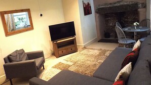 A living room with a flat-screen TV on a wooden stand, a grey sofa, a dining table with chairs, and a stone fireplace. - Tryfan Cottage  -  2.8 miles from Summit of Mt Snowdon (Beddgelert)
