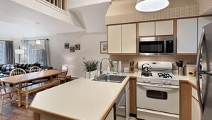 A modern kitchen with a central island, white cabinetry, and stainless steel appliances. - Woods Village 43 (Killington)