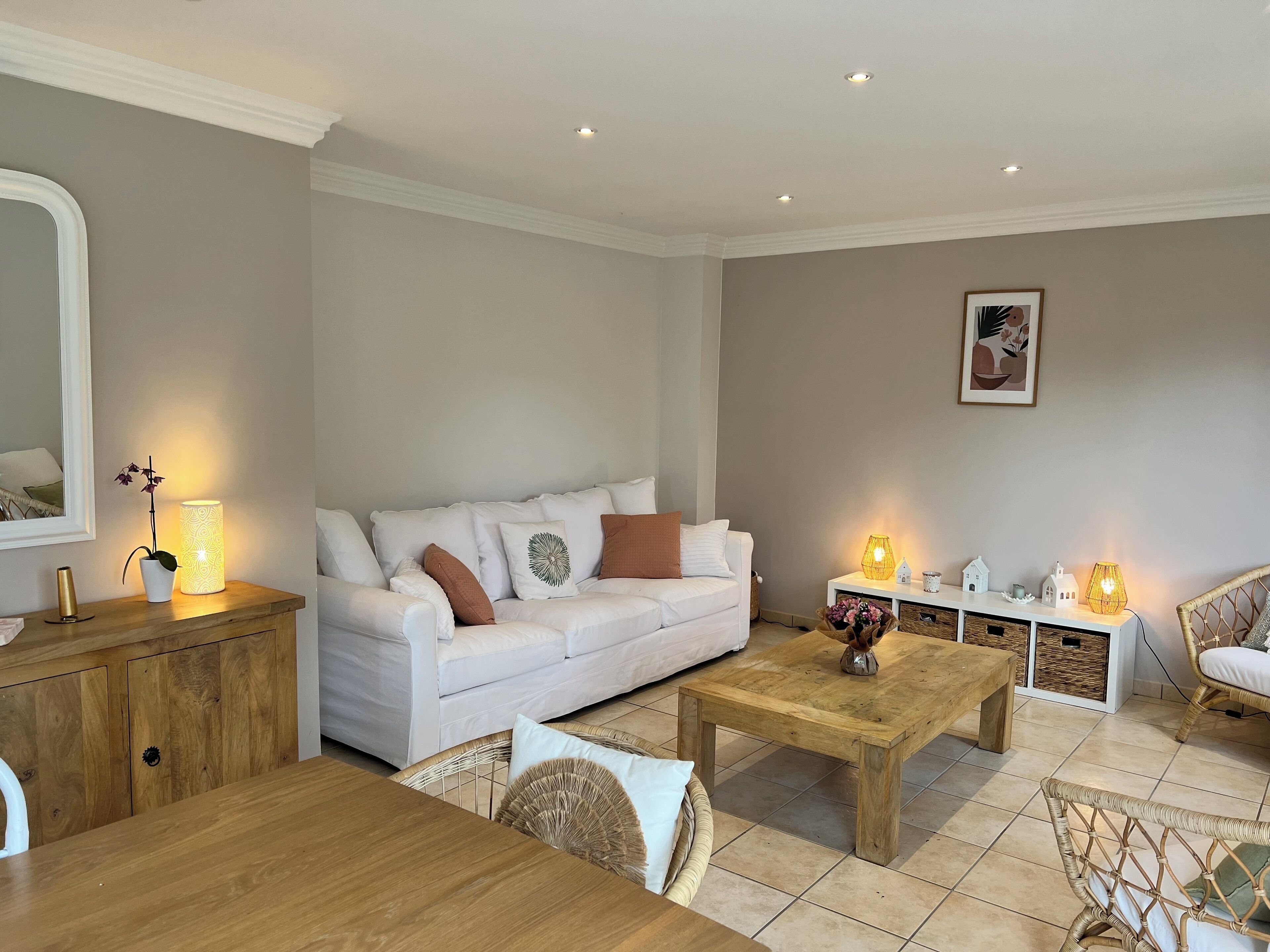 Ein modernes Wohnzimmer mit einem weißen Sofa, einem Holztisch, Korbstühlen und einem Esstisch.
