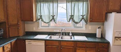 A kitchen with wooden cabinets, a double sink, and a window with curtains.