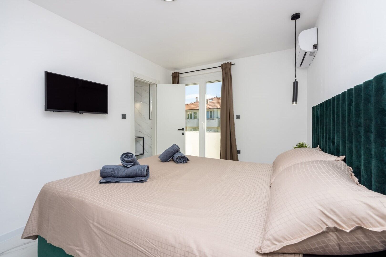 Een slaapkamer met een bed, een flatscreen-tv, een raam met gordijnen en een airconditioning.