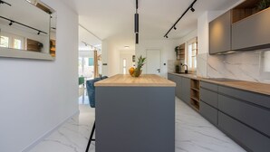 Une cuisine moderne avec un îlot central, des meubles de couleur grise et un sol en marbre.