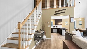 A spacious living area with a wooden staircase, a dining area, and a kitchen. - The Mendon House (Rutland)