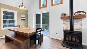 A dining area with a wooden table and benches, a hanging light fixture, and a fireplace with a stone accent wall. - The Mendon House (Rutland)