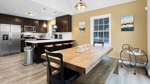 A modern kitchen with dark cabinets, a stainless steel refrigerator, a microwave, and a large island with bar stools. - The Mendon House (Rutland)