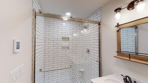 Um banheiro moderno com azulejos brancos tipo metrô, box de vidro, vaso sanitário e pia.