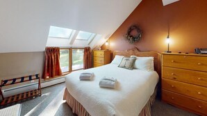 Een slaapkamer met een bed, een houten dressoir en een raam met gordijnen.