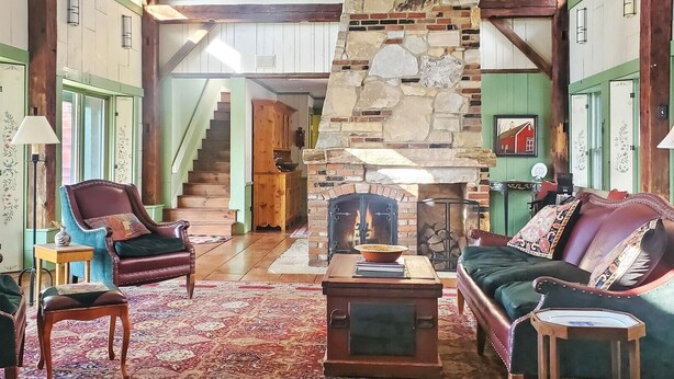 A cozy living room with a stone fireplace, leather sofas, and a staircase leading to another level. - Old Orchard House (Brandon)