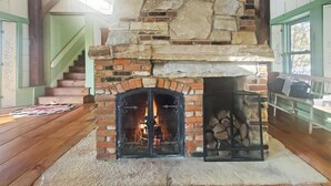 A stone fireplace with a fire, a wooden floor, and a staircase leading to an upper level. - Old Orchard House (Brandon)