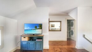 A room with a television displaying a beach scene, a blue cabinet, and a staircase leading to another room. - Old Orchard House (Brandon)