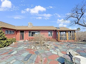 A red house with a stone-tiled patio, a chimney, and a large windowed porch. - Seacoast Sanctuary (Cape Neddick)