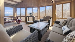 A cozy indoor seating area with wicker furniture, a wooden ceiling, and large windows offering a view of the outdoors.