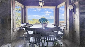 A covered outdoor dining area with a table and chairs, a hanging lantern, and a view of the ocean.