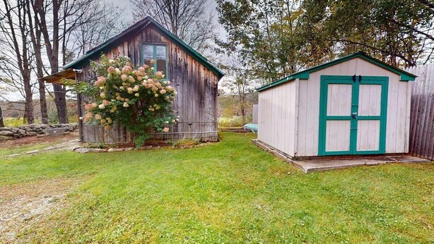Un abri de jardin rustique en bois, avec une porte verte, et un plus petit abri avec un toit vert.