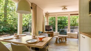 A dining area with a table set for four, a television, and a view of the garden. - Summio Parc Heihaas (Putten)