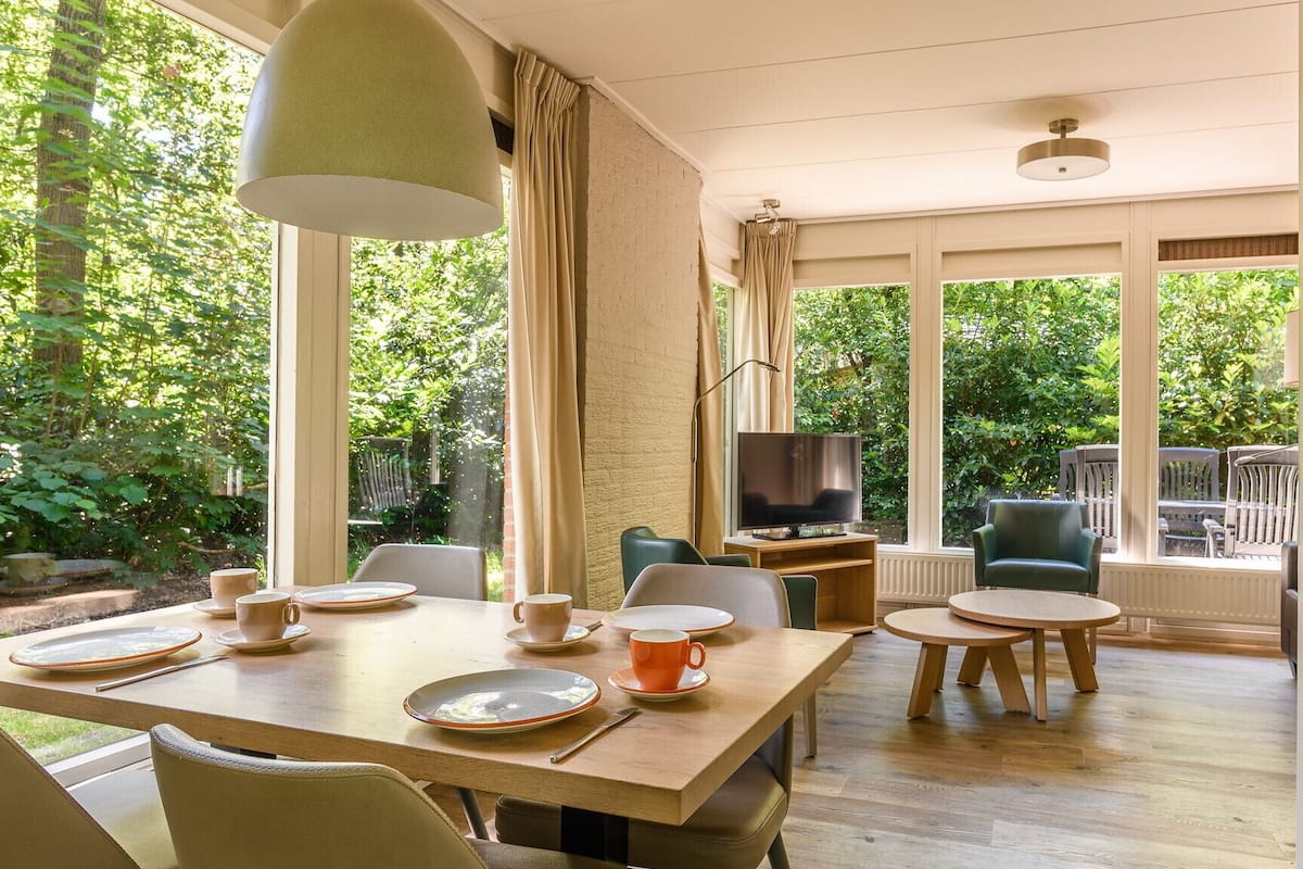 A dining area with a table set for four, a television, and a view of the garden.