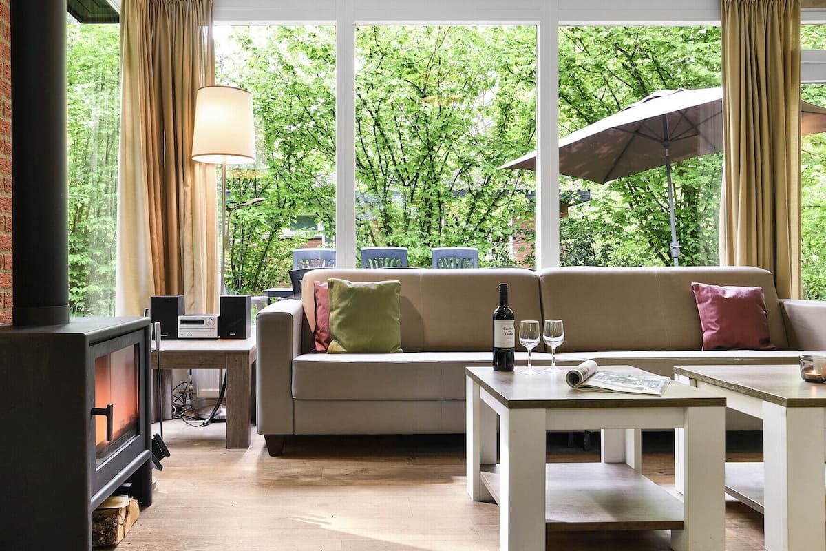 A cozy living room with a fireplace, a sofa, a coffee table, and a large window with curtains.