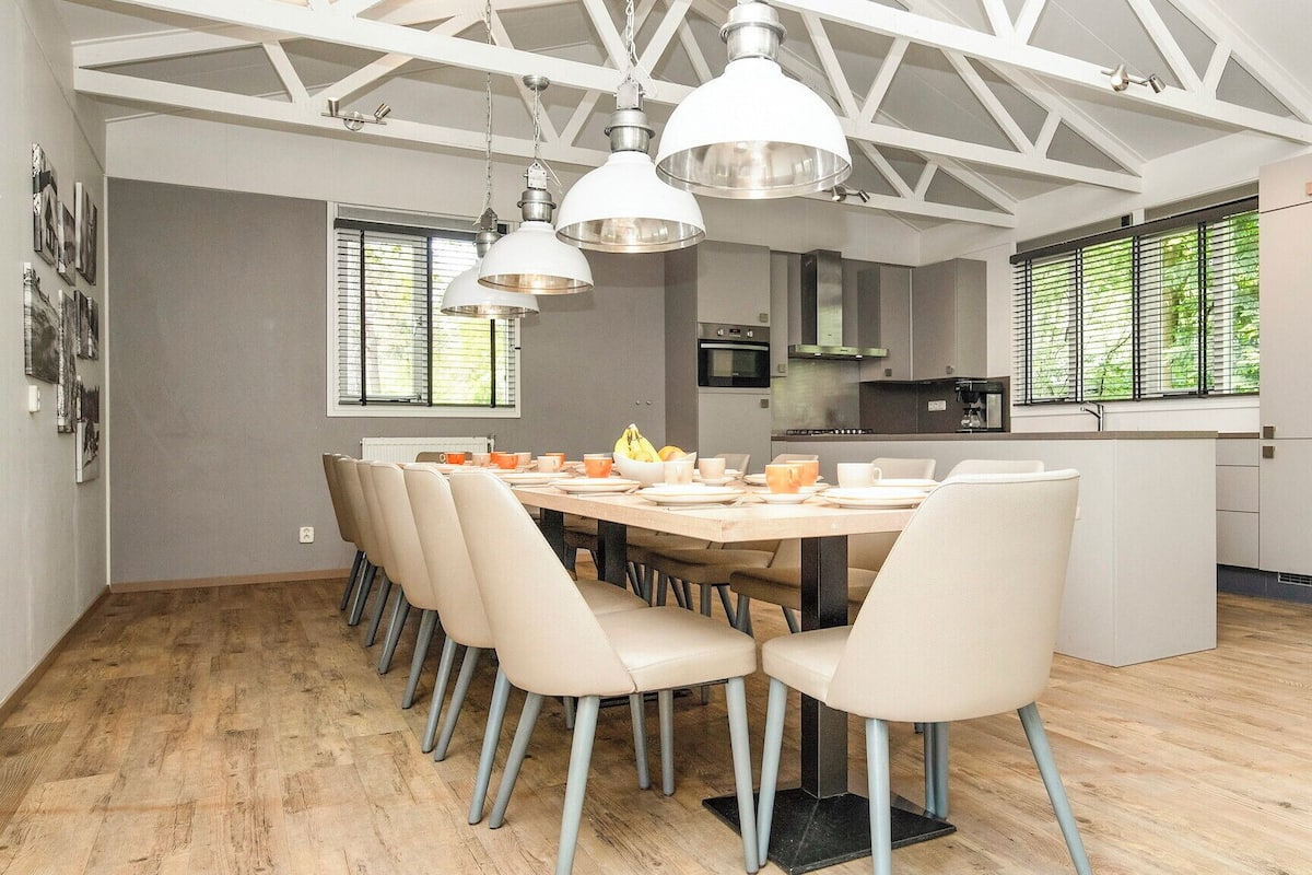 A modern kitchen with a dining area, featuring a large wooden table, beige chairs, and pendant lights.