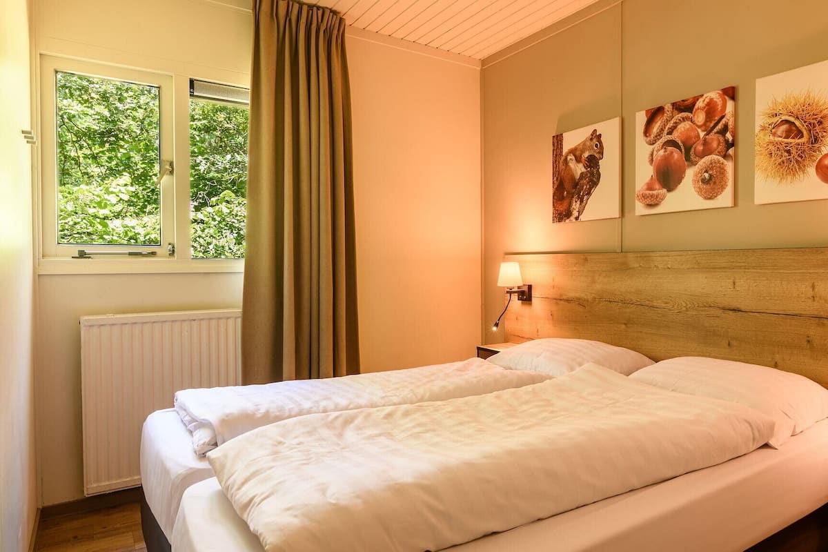 A hotel room with a large bed, two bedside tables, a window with curtains, and wall art depicting food items.