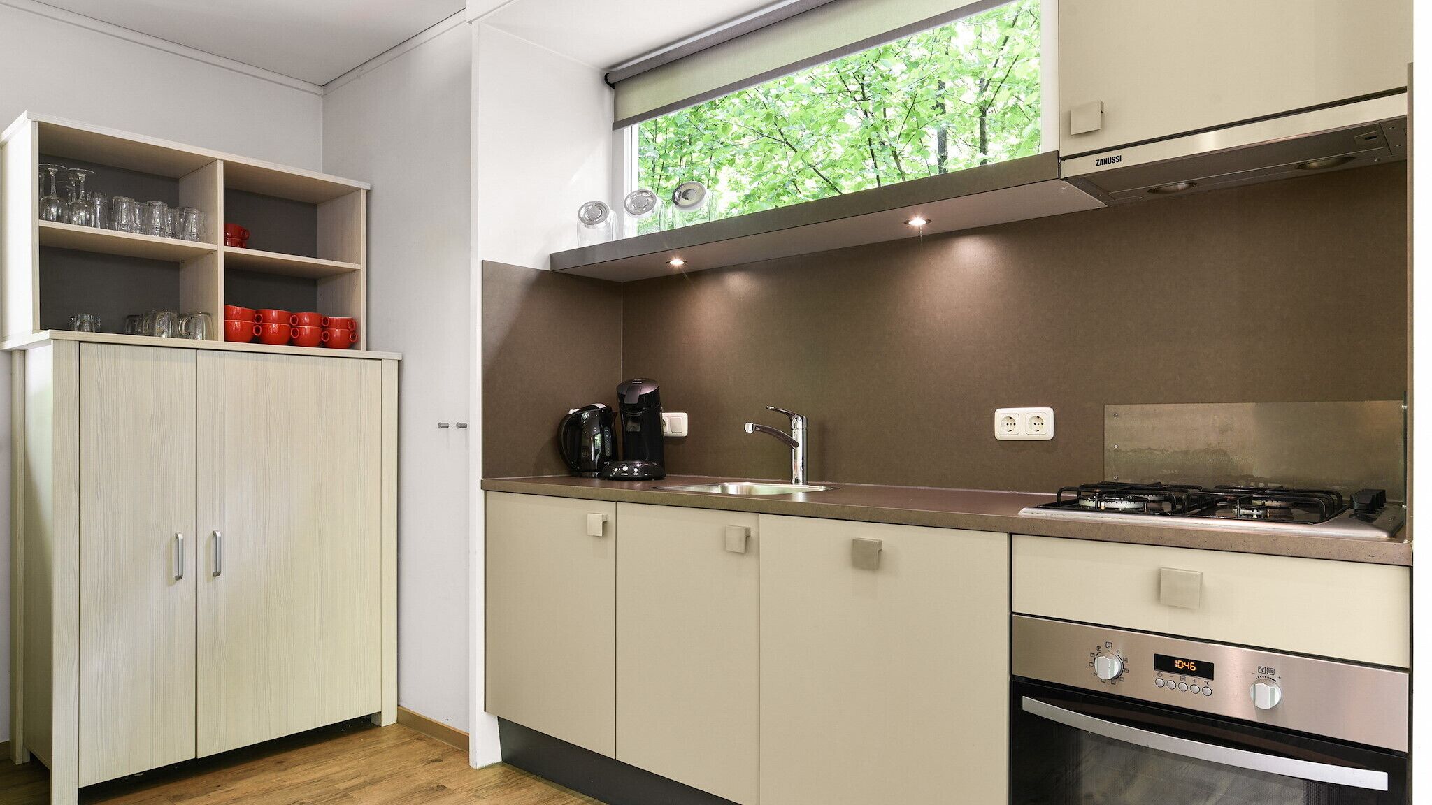 A modern kitchen with a gas stove, a coffee maker, and a sink. There are cabinets and a window above the sink.