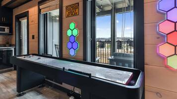 Una mesa de billar en una habitación con un cartel de precaución, un adorno de luz hexagonal y vistas al exterior.