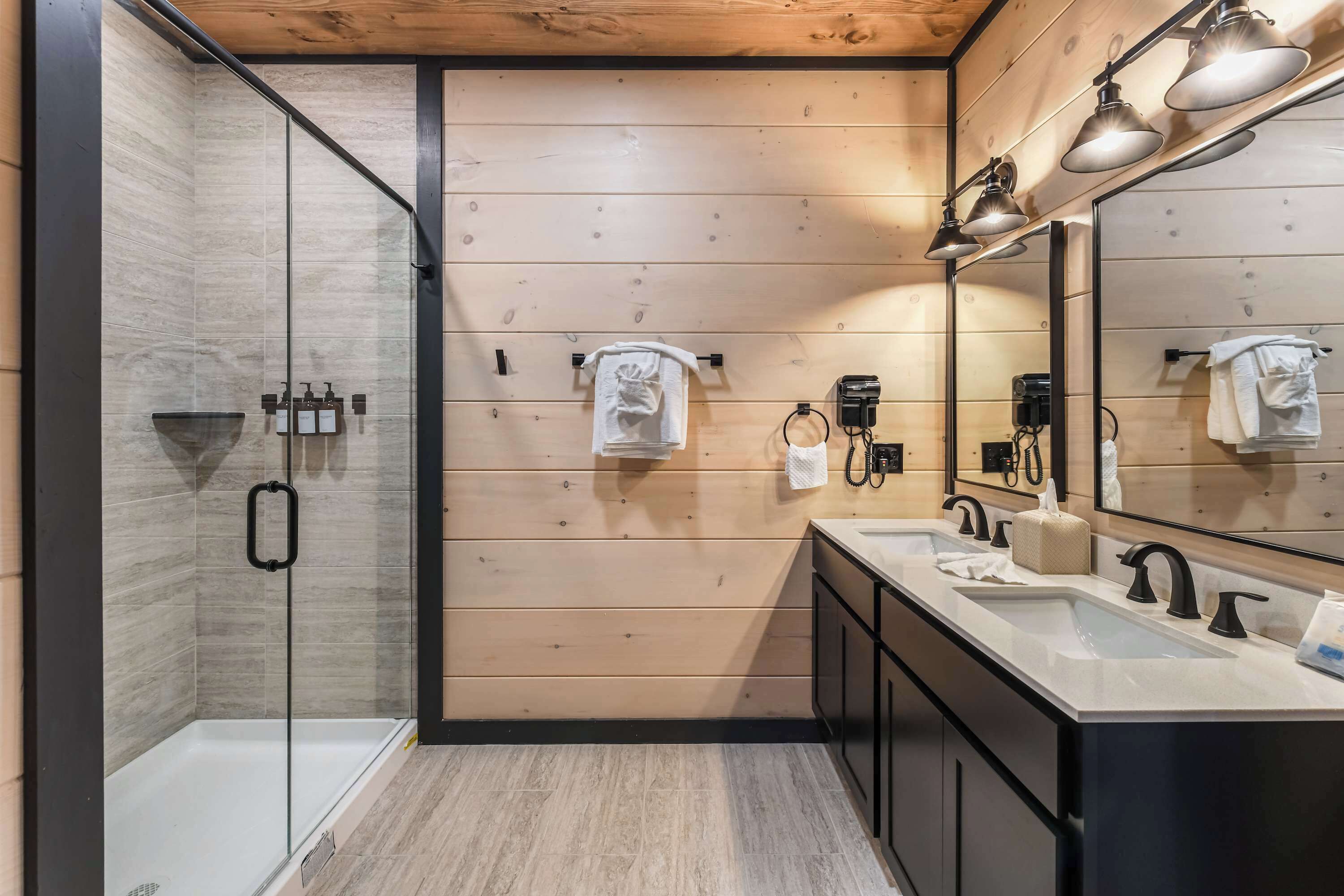 Une salle de bain moderne avec une douche à parois de verre, des murs recouverts de panneaux en bois et un grand miroir au-dessus du lavabo.
