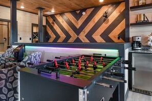 Ein Kicker steht in einem Raum mit einer Zickzack-Mauer, einer Kaffeemaschine und einem Kicker mit roten und schwarzen Spielfiguren.