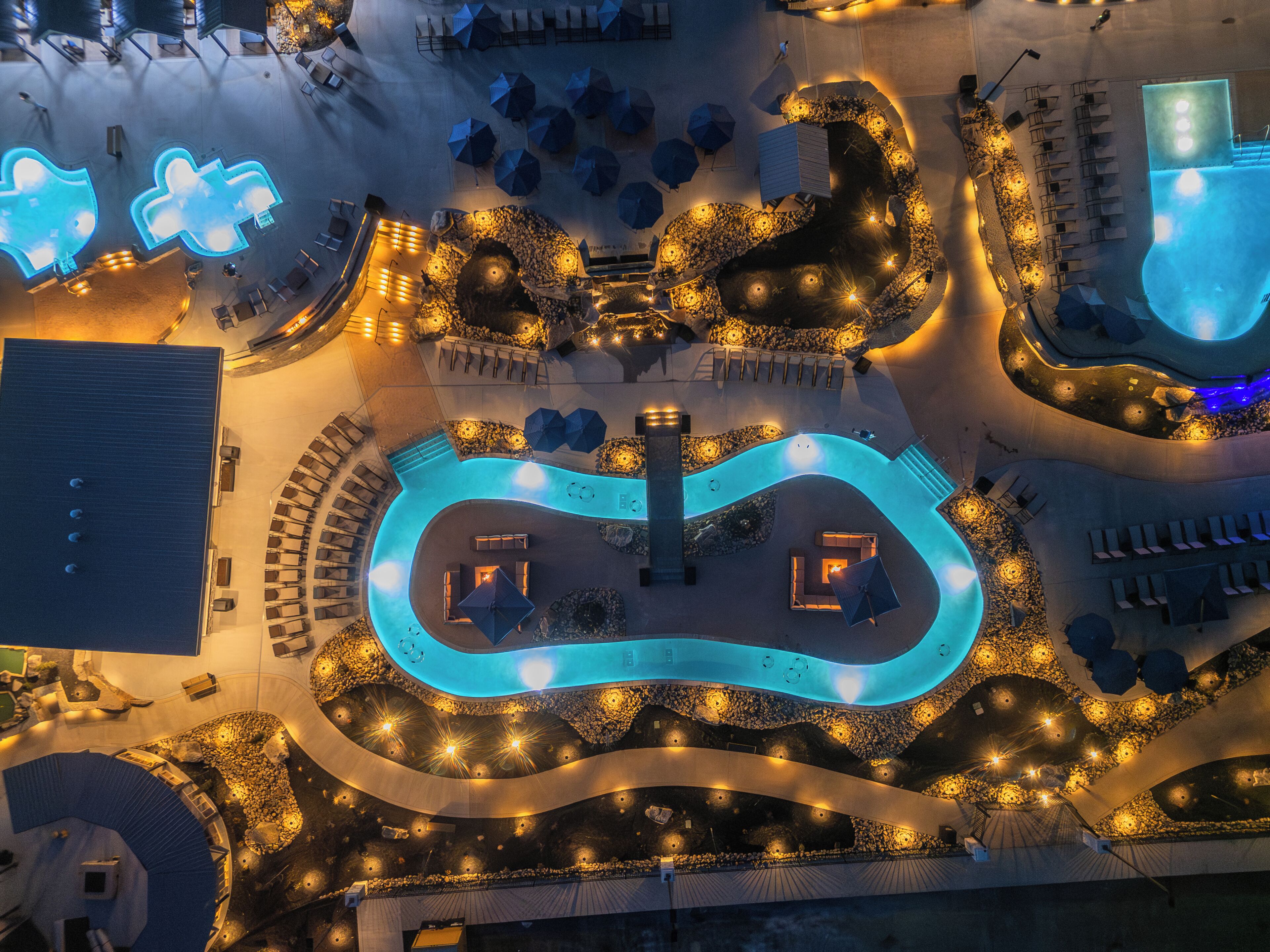 An aerial view of a resort with a winding pool, lounge areas, and outdoor seating.