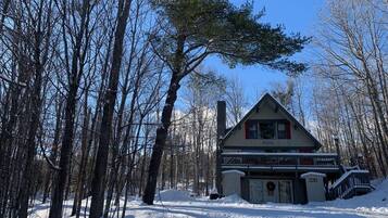 A lodge with a large porch and a chimney, surrounded by snow-covered trees.