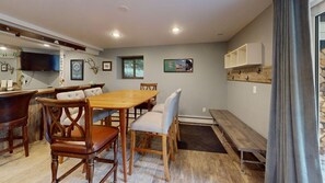 A dining area with a wooden table and chairs, a bench, and a television mounted on the wall. - Treehouse Home (Ludlow)