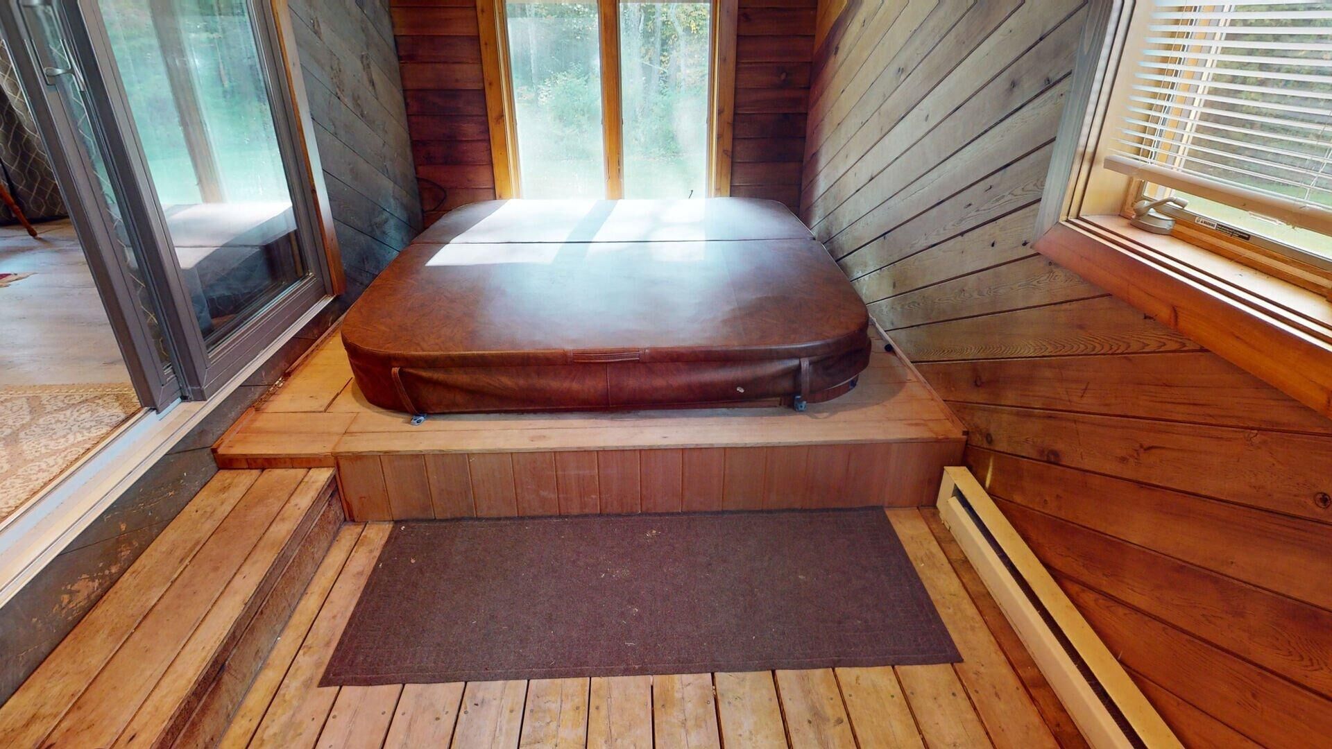 A wooden cabin interior with a raised platform, a bench, and a view through the windows.