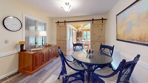 A dining area with a round glass table surrounded by wicker chairs, wooden cabinets, and a clock on the wall. - The Maple Leaf (Killington)