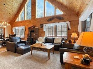 A cozy living room with wooden walls, a fireplace, and large windows. - Beechwood Home (Rutland)