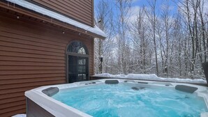A hot tub in a snowy outdoor setting with a wooden building in the background. - Beechwood Home (Rutland)