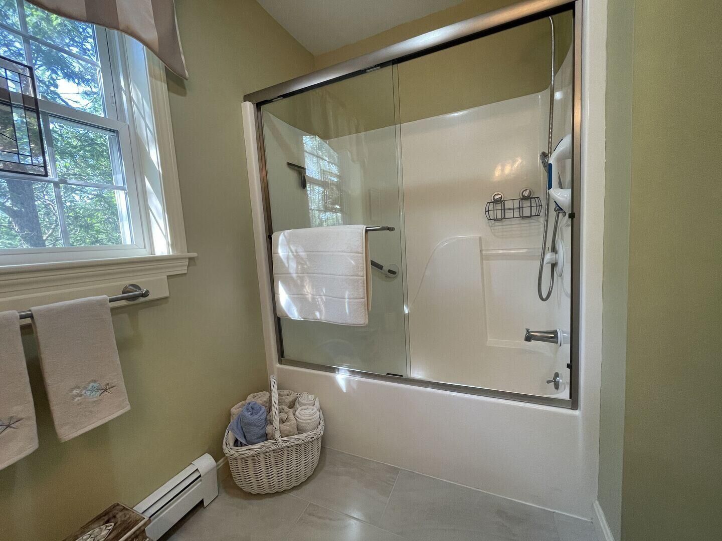 A modern bathroom with a glass-enclosed shower, a bathtub, and a window providing natural light.