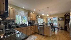 A modern kitchen with wooden cabinets, a central island, stainless steel appliances, and pendant lighting. - Harbor Hideaway (York)