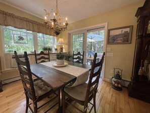 Comedor con mesa y sillas de madera, un candelabro y ventanas amplias con vistas al exterior.
