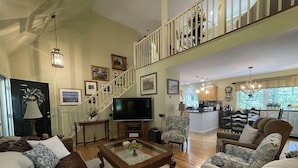 A spacious living room with a high ceiling, a staircase, a kitchen area, and a dining area. - Harbor Hideaway (York)