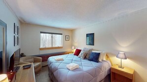 A bedroom with a large bed, a TV, a desk, and a window. - Woods Village 33 (Killington)