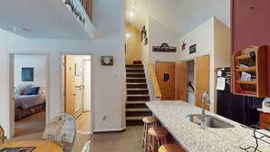 A modern kitchen with a granite countertop, a built-in sink, and a wooden staircase leading to another level. - Woods Village 33 (Killington)