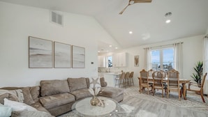 A spacious living area with a sectional sofa, a round coffee table, and a dining area with wooden chairs and a table. - The Suncatcher by Seaside Vacations & Sales (Chincoteague Island)