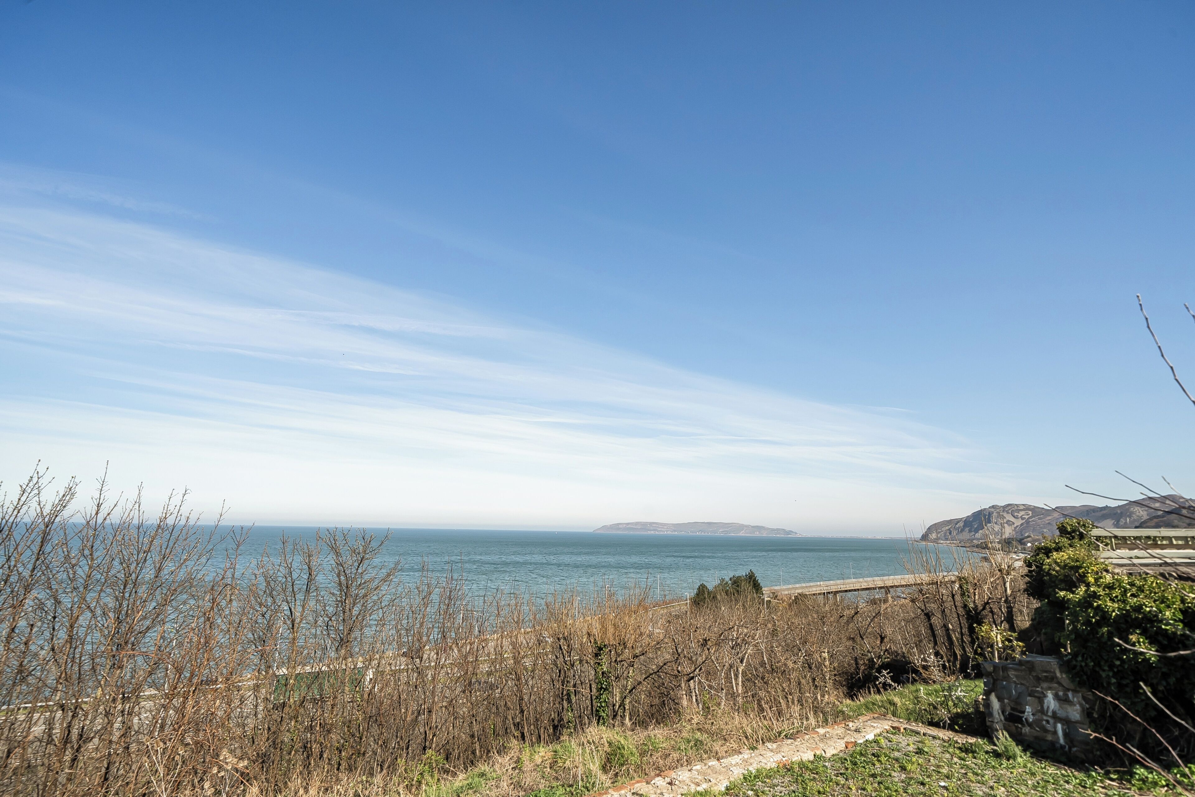 A coastal landscape with a clear sky, a body of water, and distant landforms.