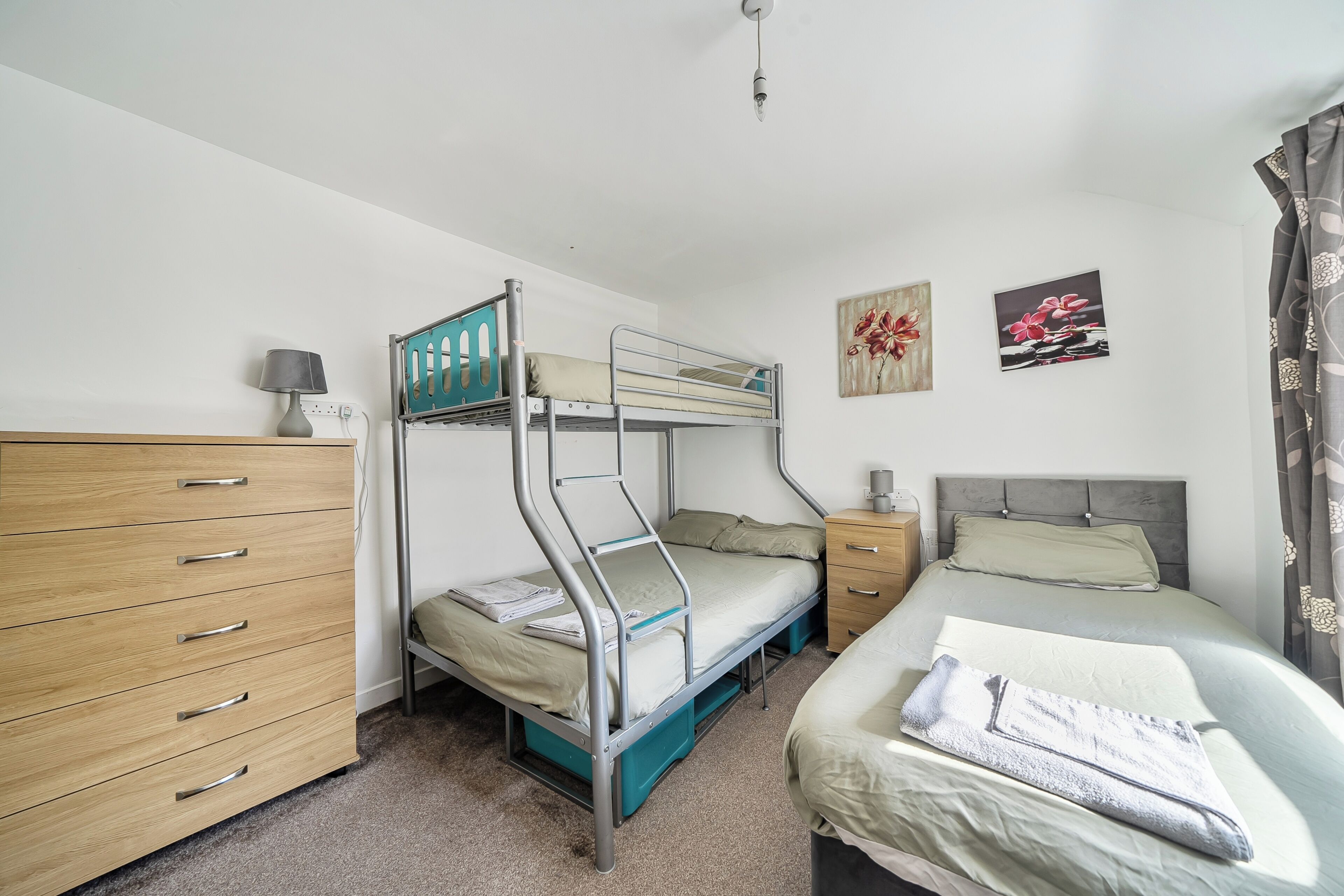 A bunk bed room with a wooden dresser, a bedside table, and two wall-mounted pictures.