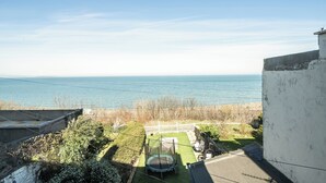 A view of a backyard with a trampoline, a white fence, and a body of water in the background. - Stunning Sea View Blue Haven in Penmaenmawr (Penmaenmawr)