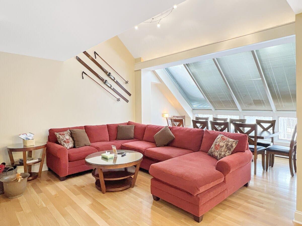 Un salon spacieux avec un canapé d’angle rouge, une table basse ronde et un coin repas comprenant des chaises et une table en bois.