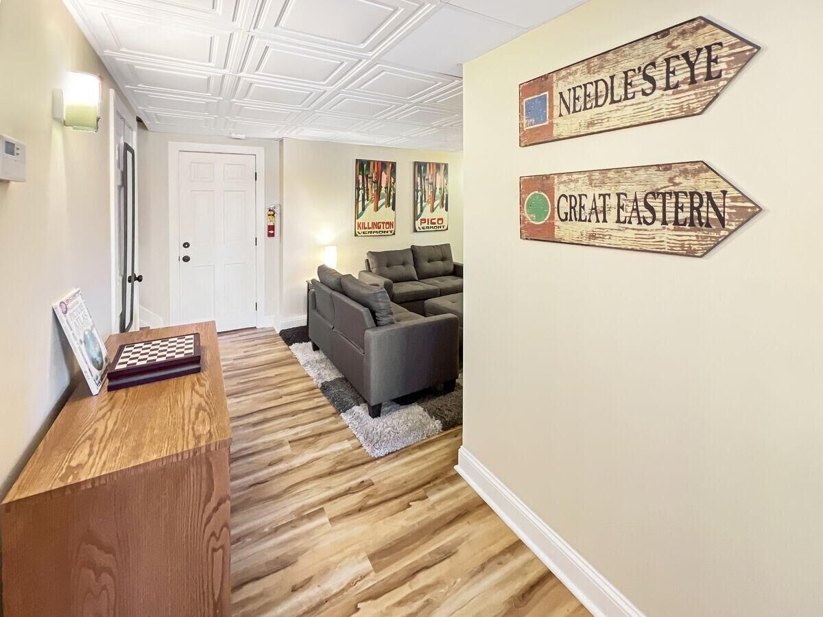 Een kamer met een houten bureau, een grijze bank en twee borden aan de muur met de tekst 'NEEDLE'S EYE' en 'GREAT EASTERN'.