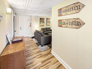 A room with a wooden desk, a grey sofa, and two wall signs reading "NEEDLE'S EYE" and "GREAT EASTERN".