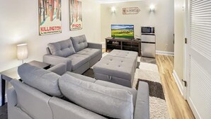 Ein modernes Wohnzimmer mit grauen Sofas, einem Fernseher und einem Kühlschrank.