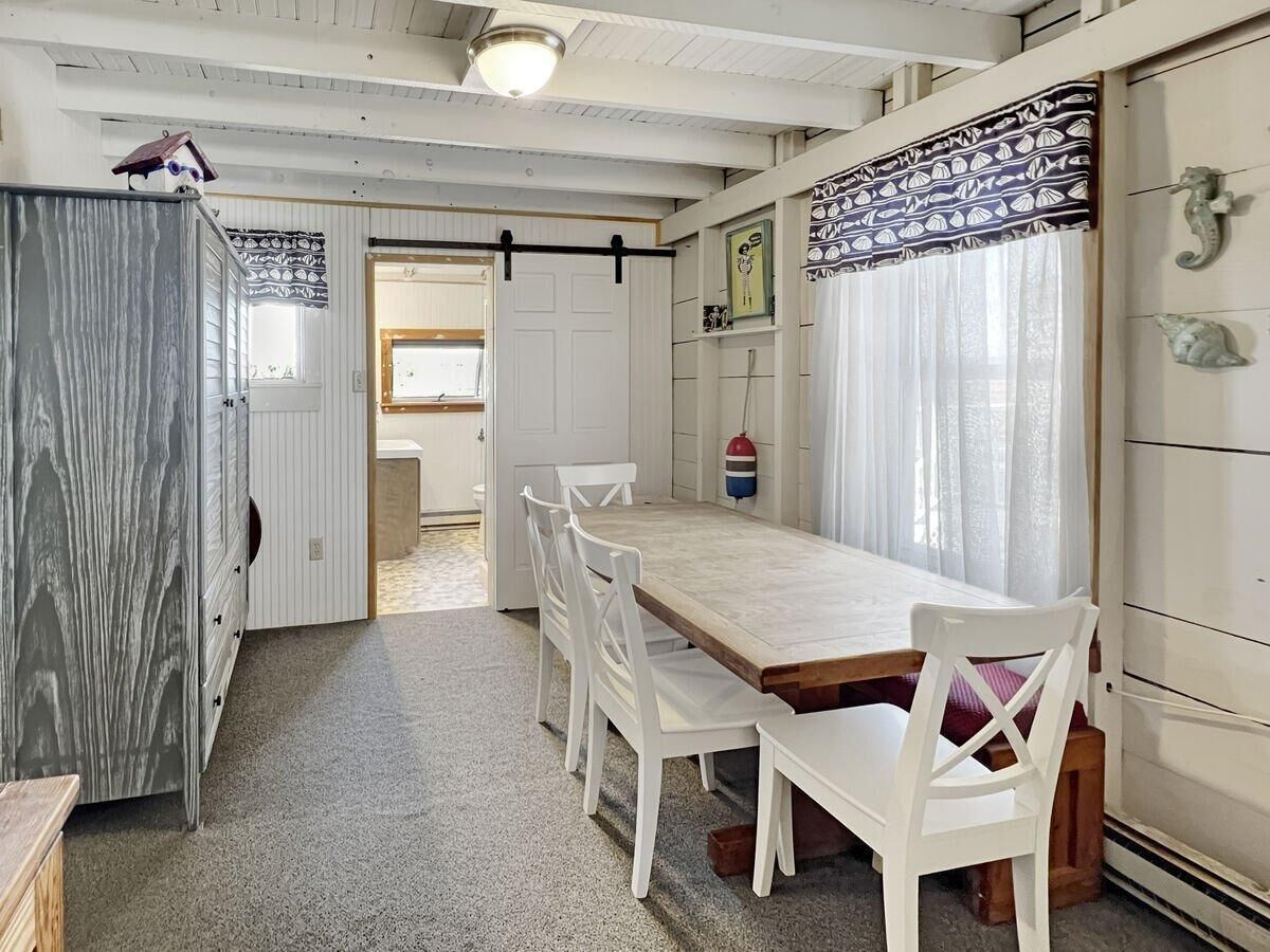 Eine kleine Küche mit einem Holztisch und weißen Stühlen, einem Kühlschrank und einem Fenster mit durchsichtigen Vorhängen.